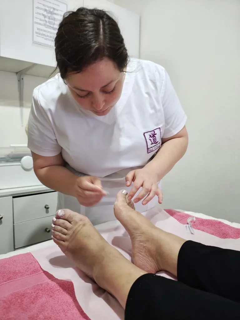 Alumno aplicando agujas de acupuntura en los puntos de los pies de un paciente.