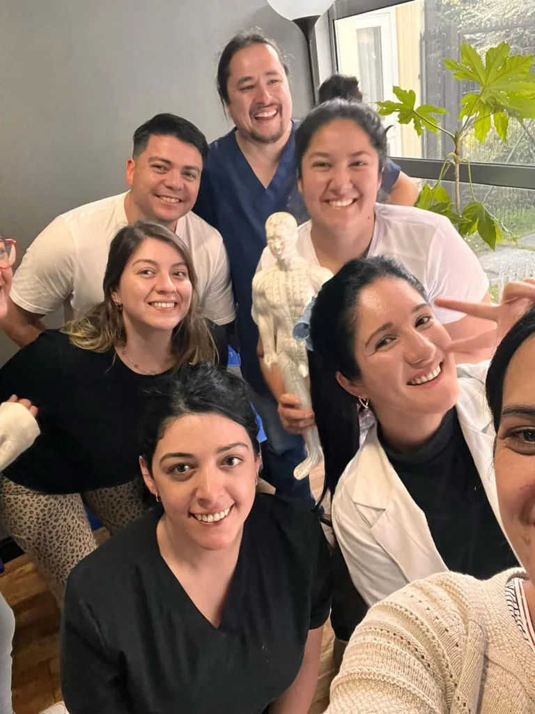 Grupo de alumnos y docentes sonriendo junto a un modelo anatómico de puntos de acupuntura.
