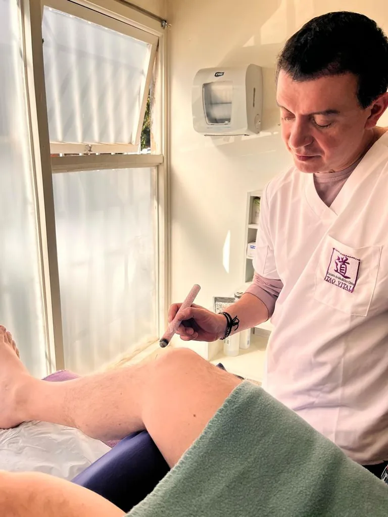 Docente aplicando moxibustión con un puro de moxa sobre la rodilla de un paciente.