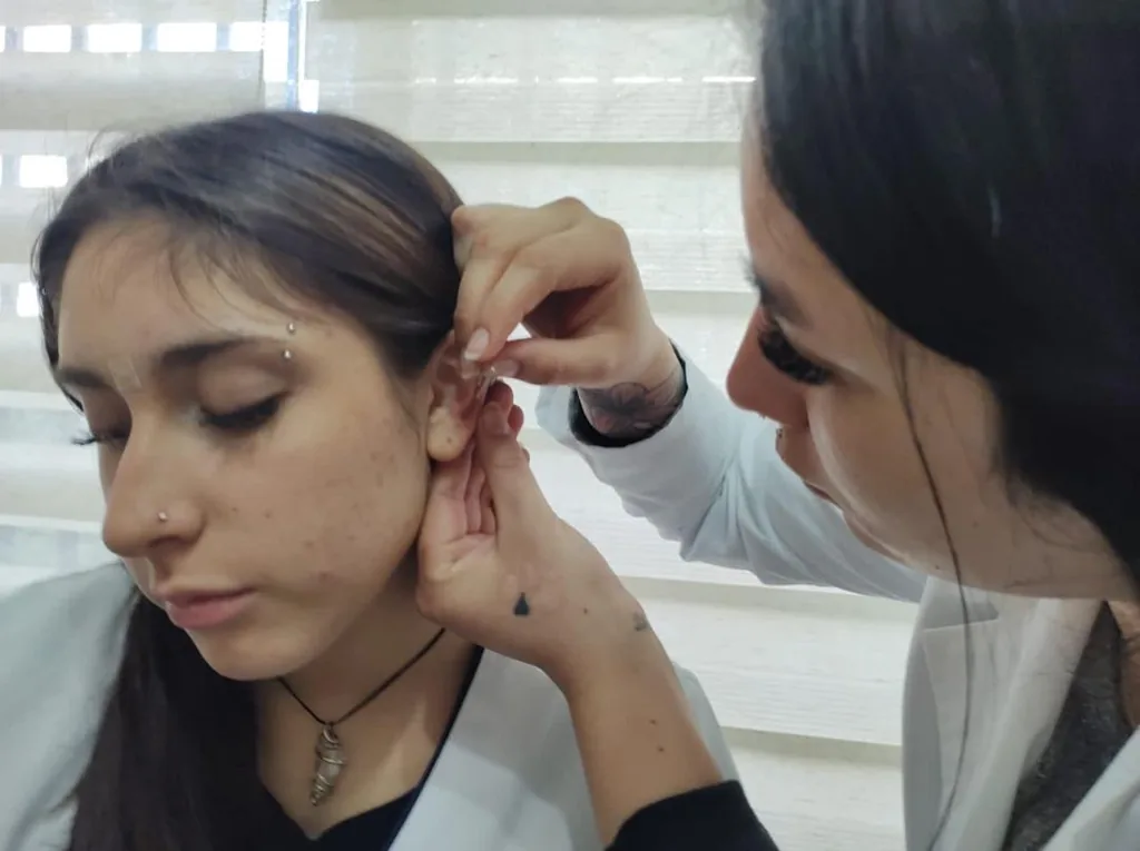 Tutora localizando puntos auriculares con un instrumento de presión en la oreja de una alumna.