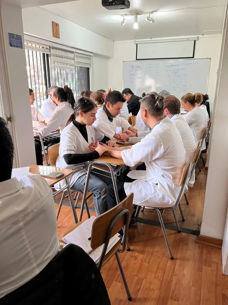 Alumnos en sala de clases iniciando el módulo de los cuatro métodos de diagnóstico, tomando el pulso a un compañero.
